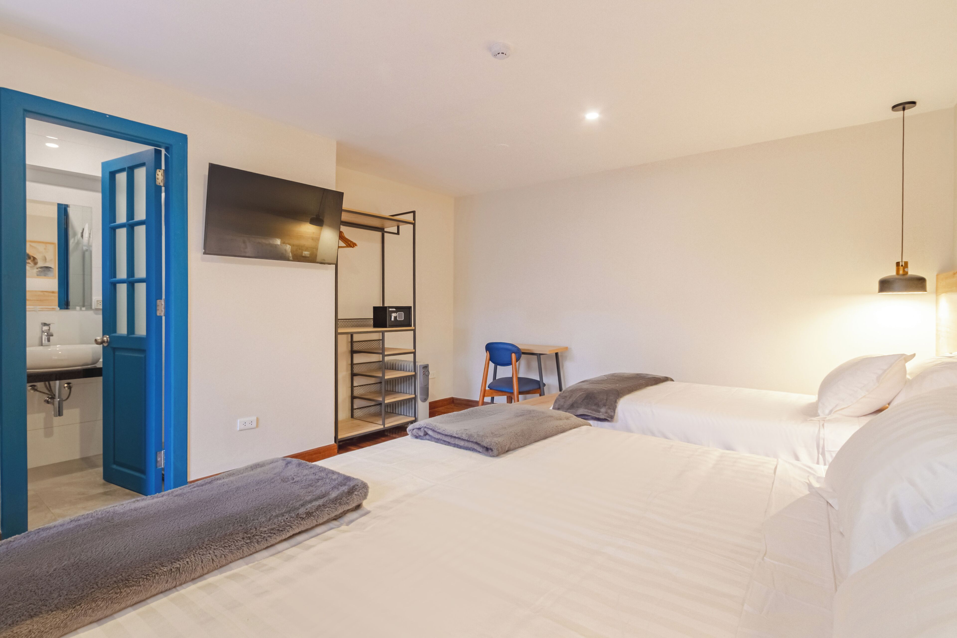 A hotel room with two beds, a desk, a chair, a TV, and a bathroom visible through an open door.