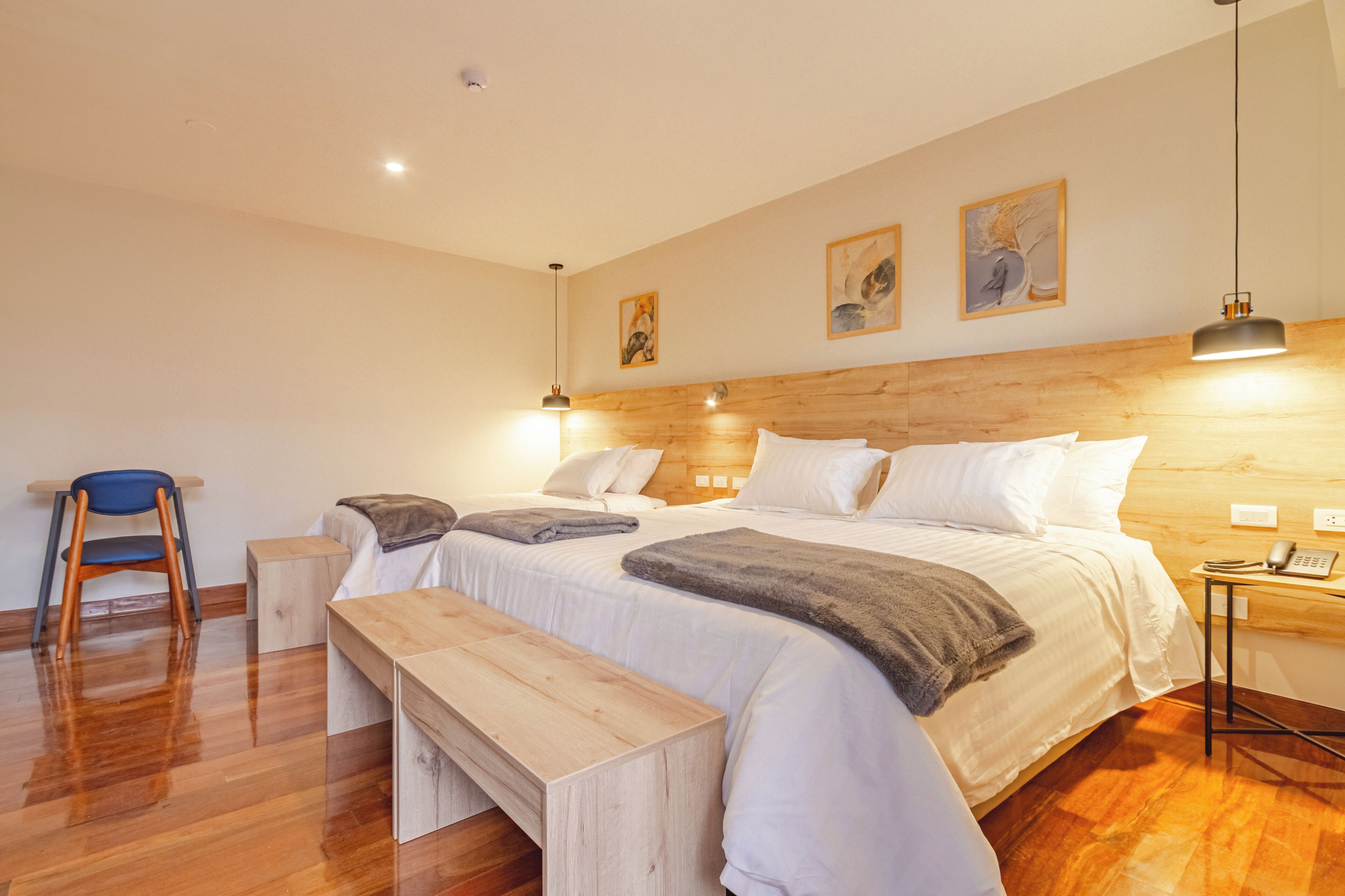 A bedroom with a wooden headboard, a bed with white linens, a bench, a chair, and a bedside table with a phone.