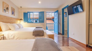 Un dormitorio con dos camas, cabeceros de madera, un banco, un televisor y un baño visible a través de una puerta abierta.