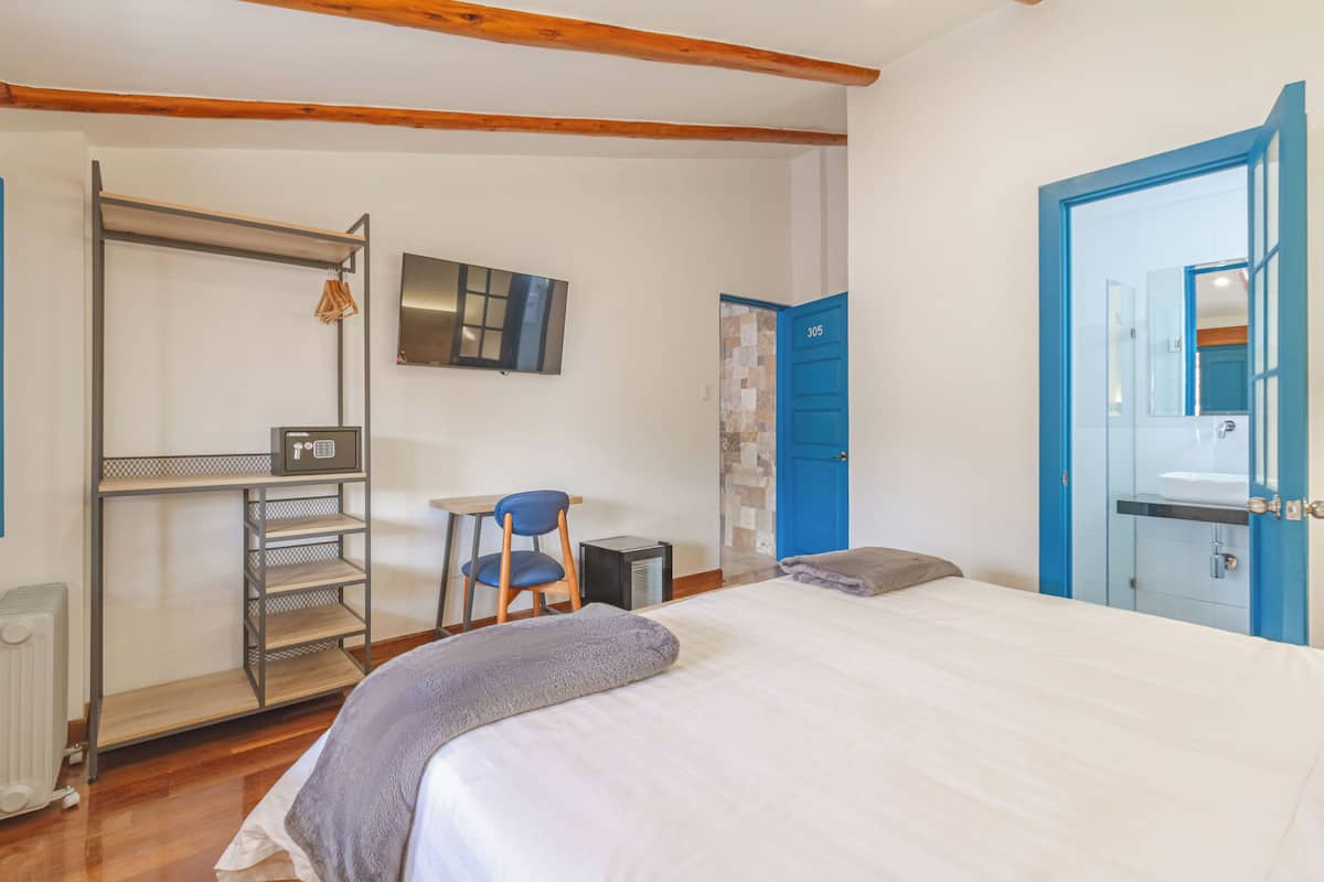 Quarto com cama, escrivaninha, cadeira, radiador, televisão e guarda-roupa.