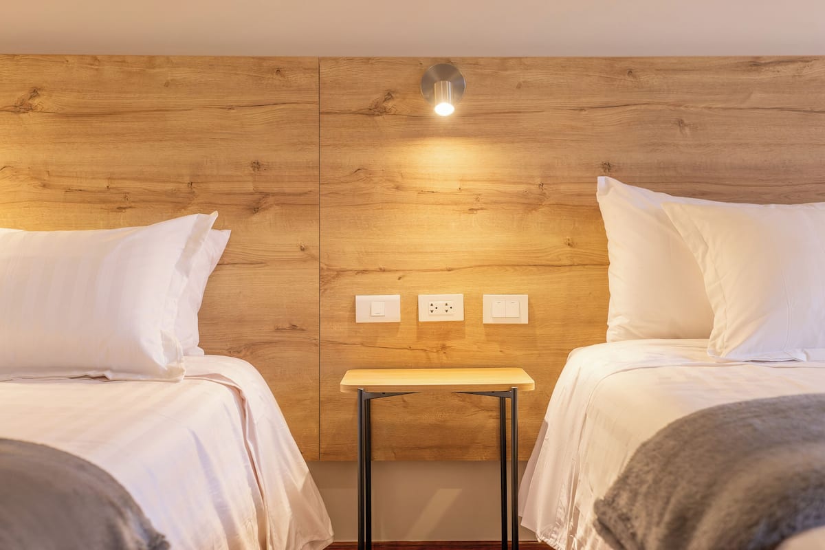 Quarto de hotel com duas camas, uma mesa pequena e cabeceira de madeira.