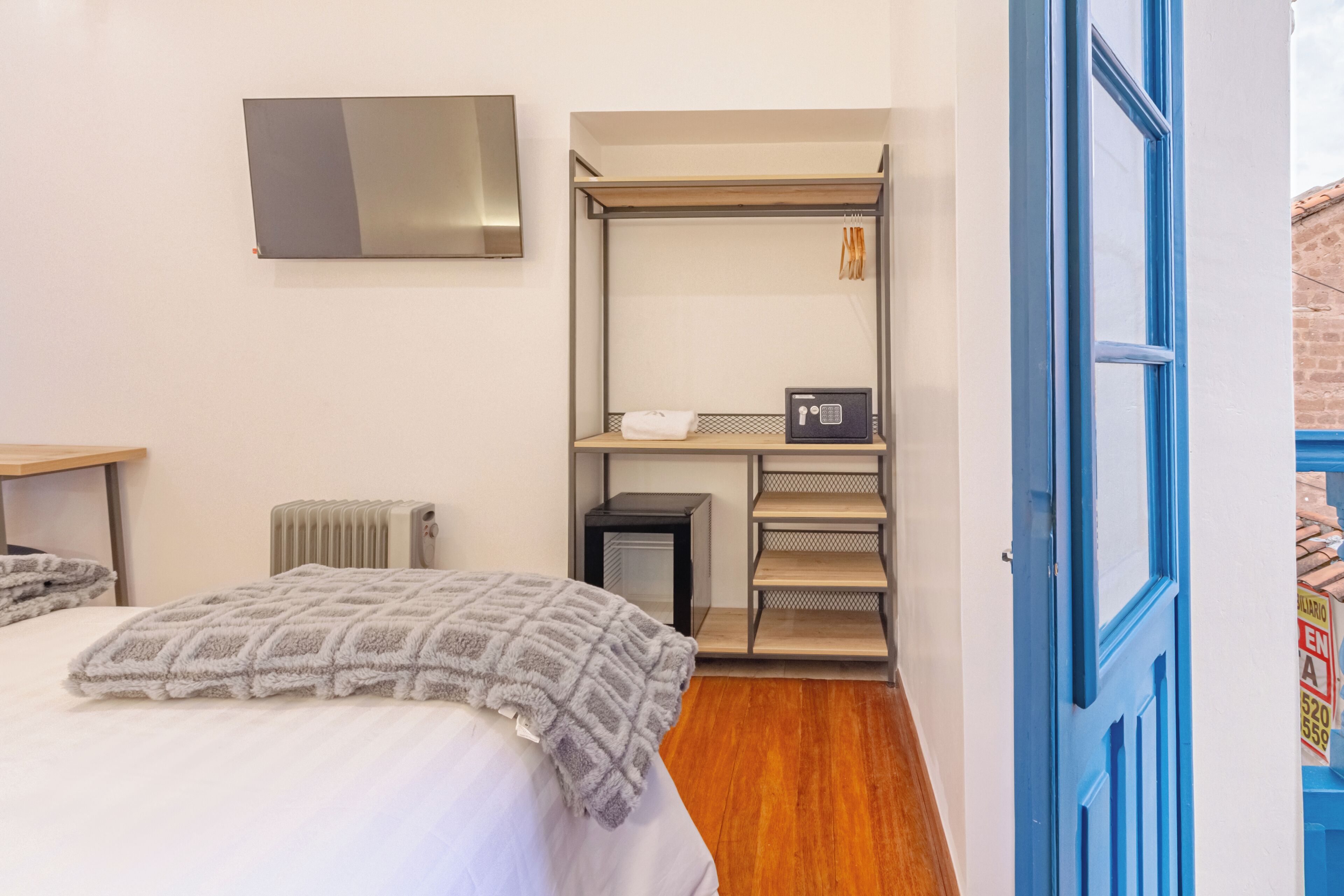 A bedroom with a bed, a radiator, a desk, a wardrobe, and a blue door.