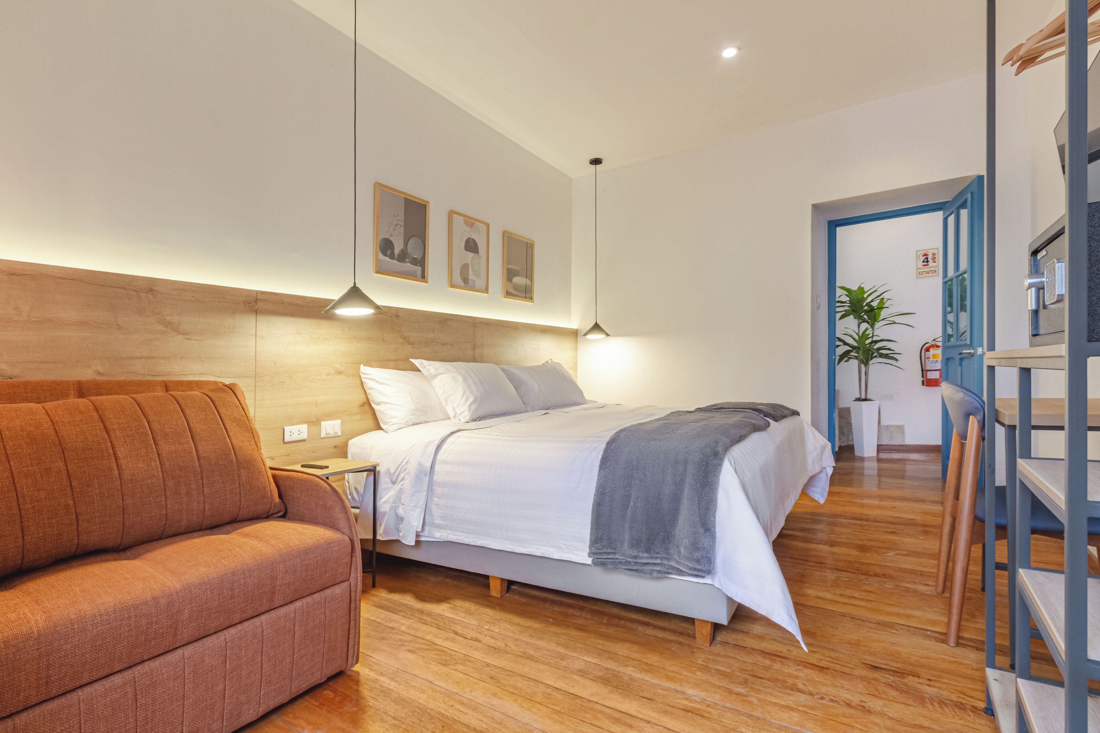 A bedroom with a bed, a sofa, a wooden floor, and a blue door.