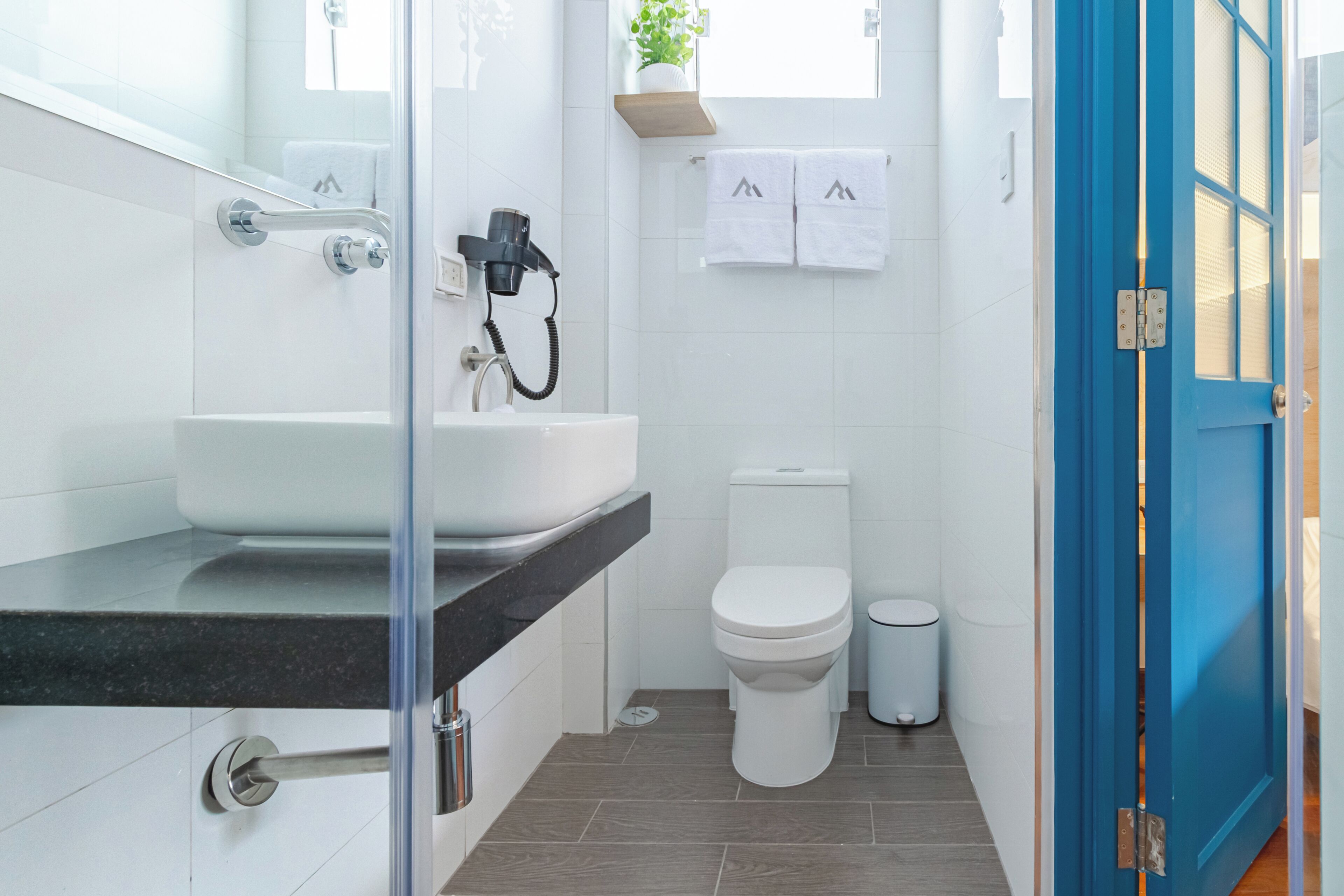 A bathroom with a white sink, toilet, and trash can, a hairdryer, and a blue door.