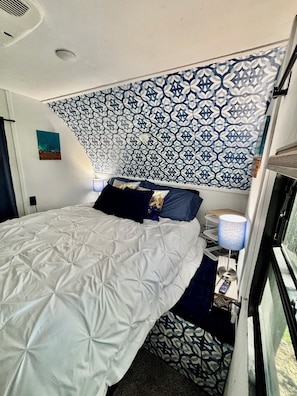 A bed with a patterned headboard, a bedside lamp, and a small table with a remote control.
