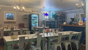 Interior de restaurante con suelos de madera, sillas y mesas de metal, un letrero de neón y un refrigerador.