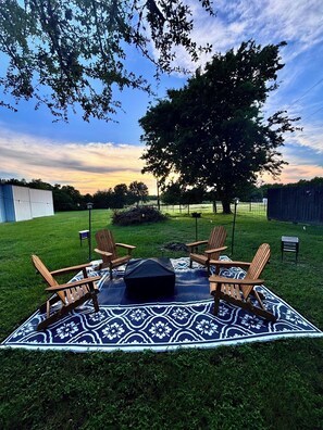 A backyard with a picnic setup including a blanket, chairs, and a fire pit.