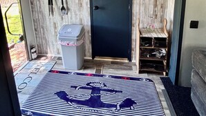 Habitación pequeña con una puerta oscura, un cubo de basura, un cartel de bienvenida, un perchero y una ventana con vistas a la vegetación.
