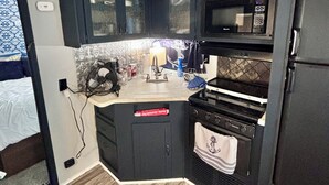 Cocina compacta con armarios oscuros, un microondas, una estufa y una encimera pequeña.