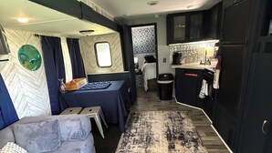 Interior compacto de autocaravana con kitchenette, sofá, mesita y alfombra estampada.