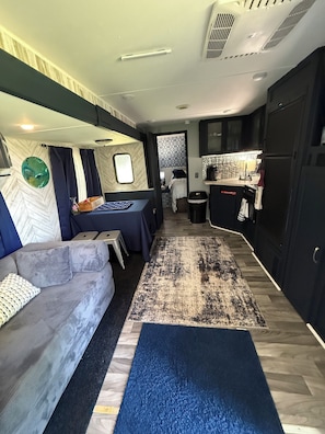 En rummelig indretning i en autocamper med et tekøkken, en sofa, et lille bord og en tæppe med mønster.