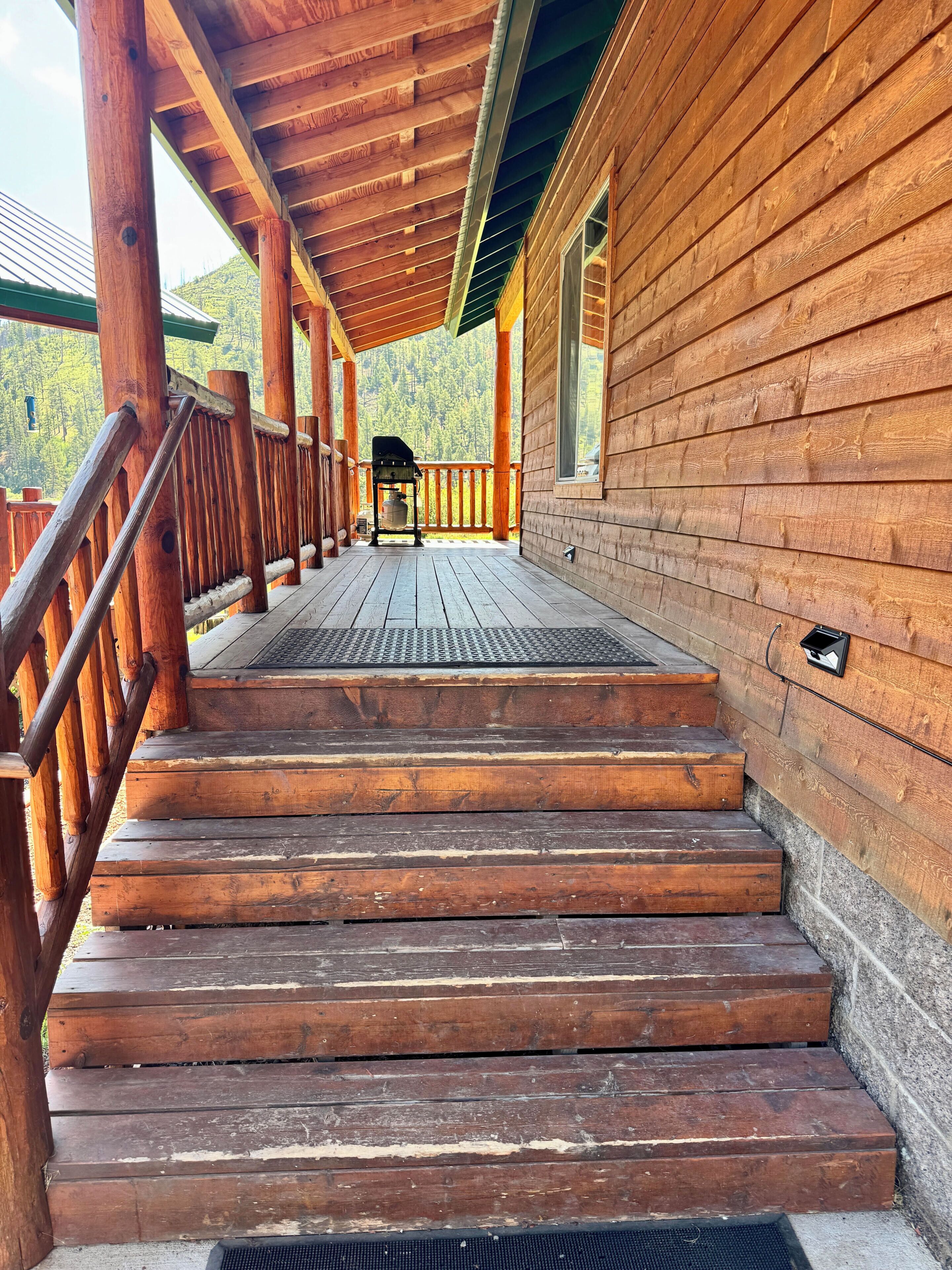 A wooden staircase leading to a covered porch with a view of a forested area.