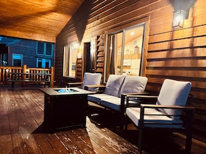 A wooden deck with a fire pit, two cushioned chairs, and a bench.
