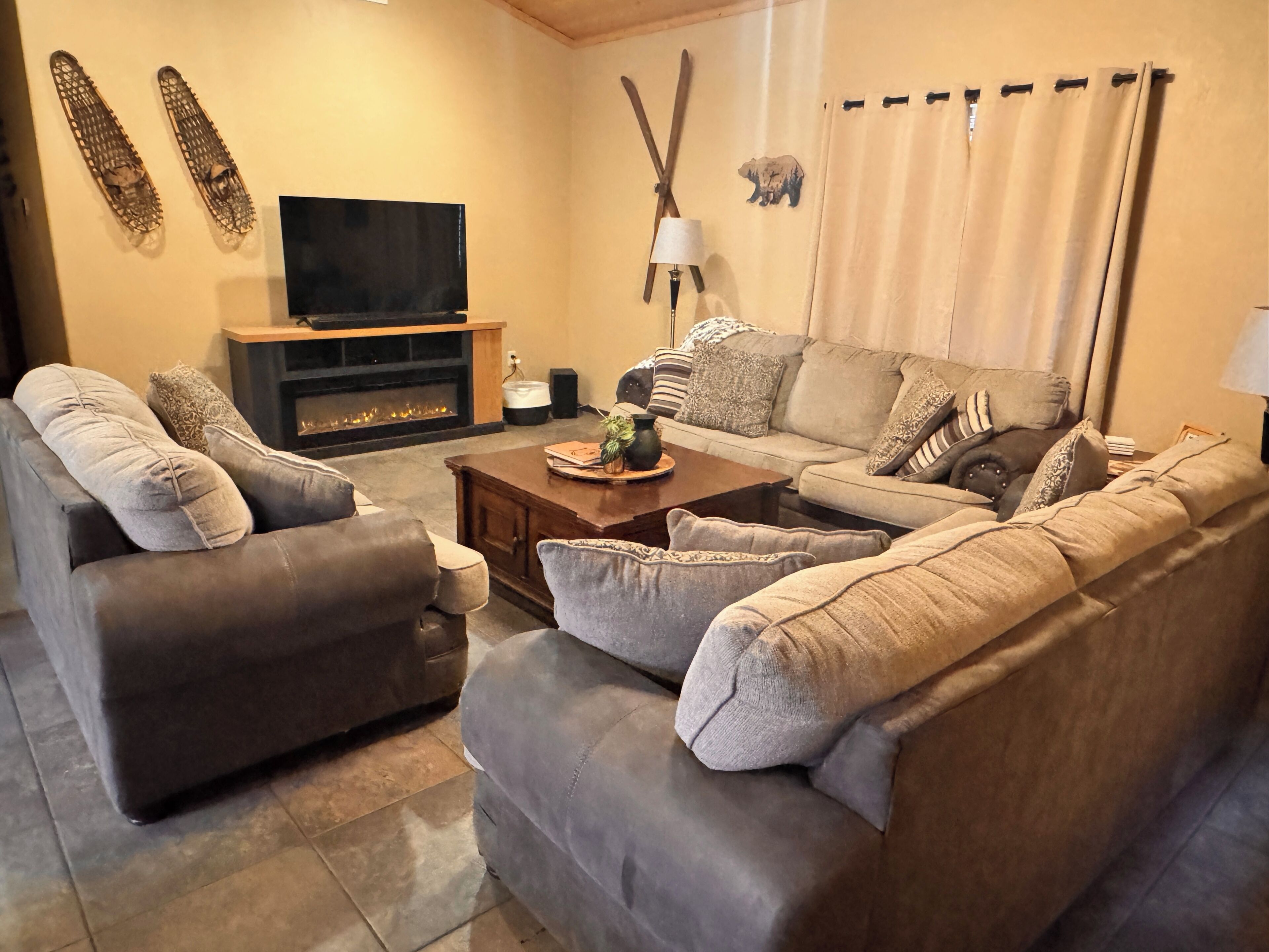 A living room with a sofa, armchairs, a coffee table, a fireplace, a television, and a wall-mounted lamp.