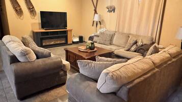 A living room with a sofa, armchairs, a coffee table, a fireplace, a television, and a wall-mounted lamp.