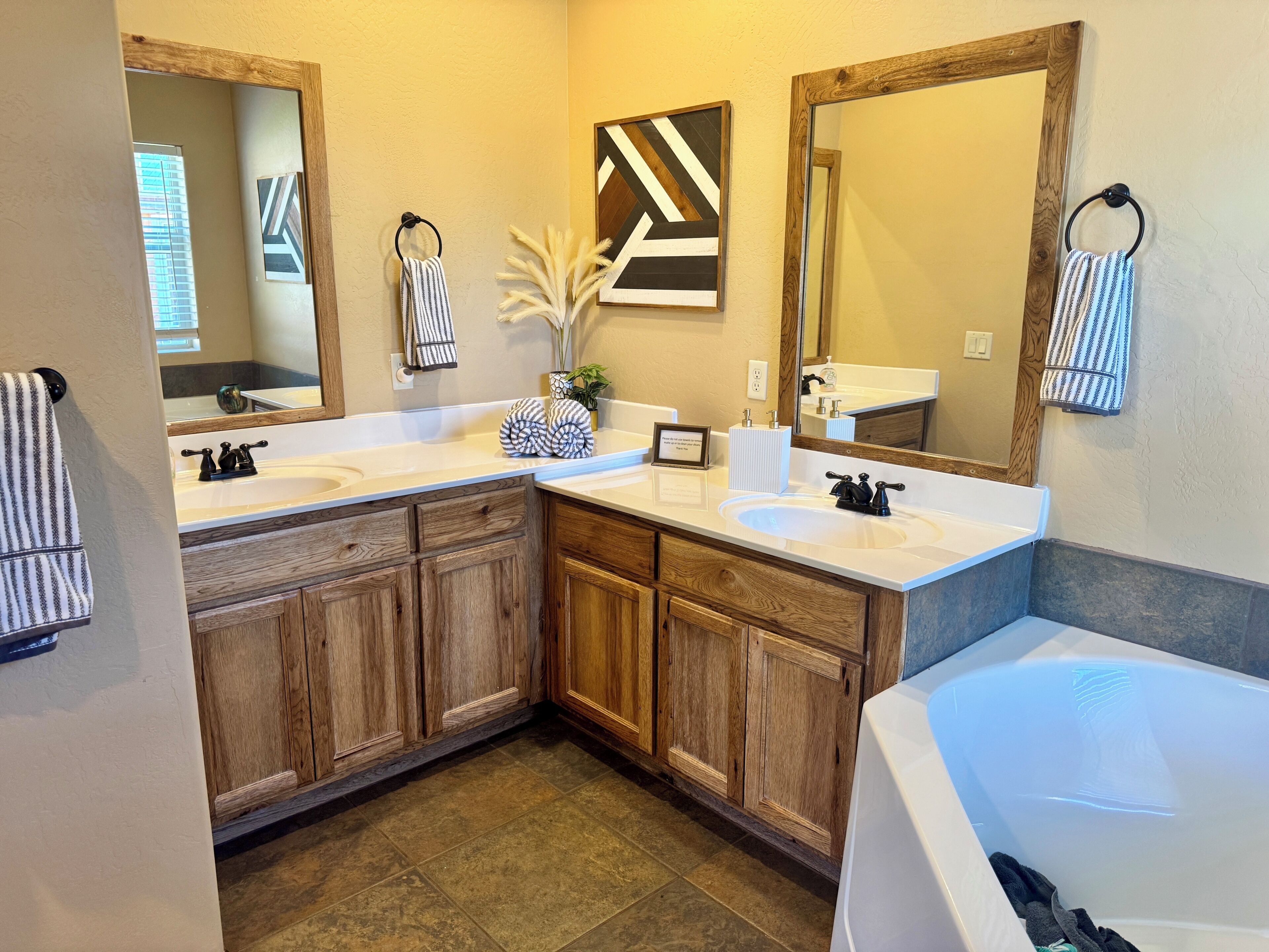 A bathroom with two sinks, wooden cabinets, a large mirror, and a bathtub.