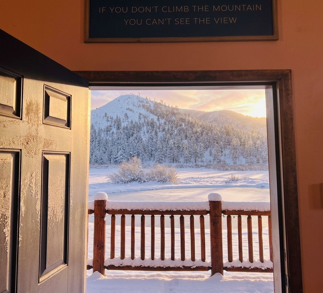 A door leading to a snowy landscape with a mountain view and a wooden fence.