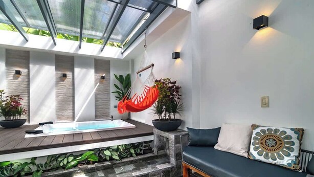 A modern indoor pool area with a hammock, seating, and potted plants. - Calla House Arenal 3BR (La Fortuna)