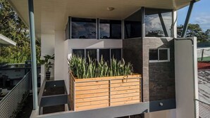 A modern building with a covered outdoor area, a wooden planter with plants, and a stone wall. - Calla House Arenal 3BR (La Fortuna)