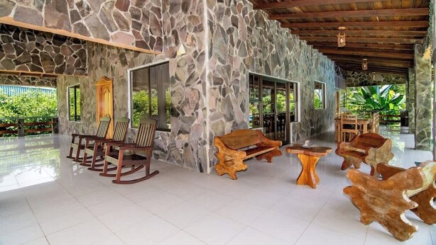 Un interior espacioso con pared de piedra, muebles de madera y vistas al exterior con vegetación.