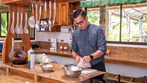 Una cocina con armarios de madera, encimera de granito y diferentes utensilios colgando.