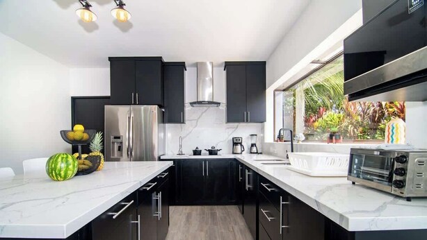 A modern kitchen with black cabinets, a stainless steel refrigerator, a microwave, and a large window with a view of greenery. - Volcano-Lux Arenal 3BR House (Tanque)