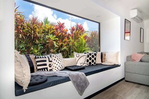 Ein modernes Wohnzimmer mit einer eingebauten Bank, einem grauen Sofa und einem großen Fenster mit Blick auf einen Garten.