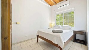 A bedroom with a bed, a window with a view, a wooden ceiling, and a small bedside table. - Casa Marea Tamarindo (Tamarindo)