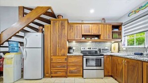 A kitchen with wooden cabinets, a refrigerator, an oven, and a window with a view. - Casa Marea Tamarindo (Tamarindo)