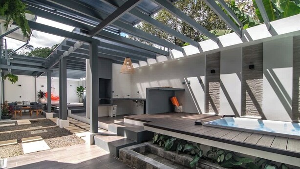 A modern outdoor patio with a wooden deck, a built-in hot tub, and a pergola structure. - La Fortuna Duo Retreat Villa 6BR (La Fortuna)