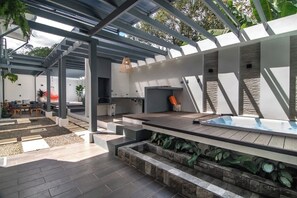 Een modern terras buiten met een houten dek, een ingebouwd whirlpool en een pergola.