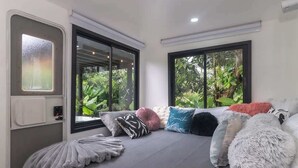 Een moderne kamer met een bed, grote ramen en uitzicht op groen.