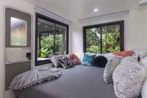 Ein modernes Zimmer mit Bett, großen Fenstern und Blick auf Grünflächen.