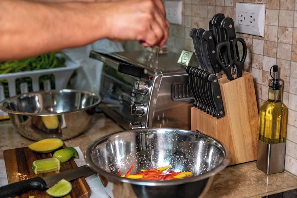 Una cocina con un tostador, una tabla de cortar con fruta en rodajas, un tazón de metal y un cuchillo.