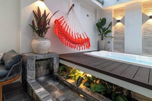 Ein modernes Badezimmer mit einer freistehenden Badewanne, einer Steinwand und einem hängenden Makramee-Sessel.