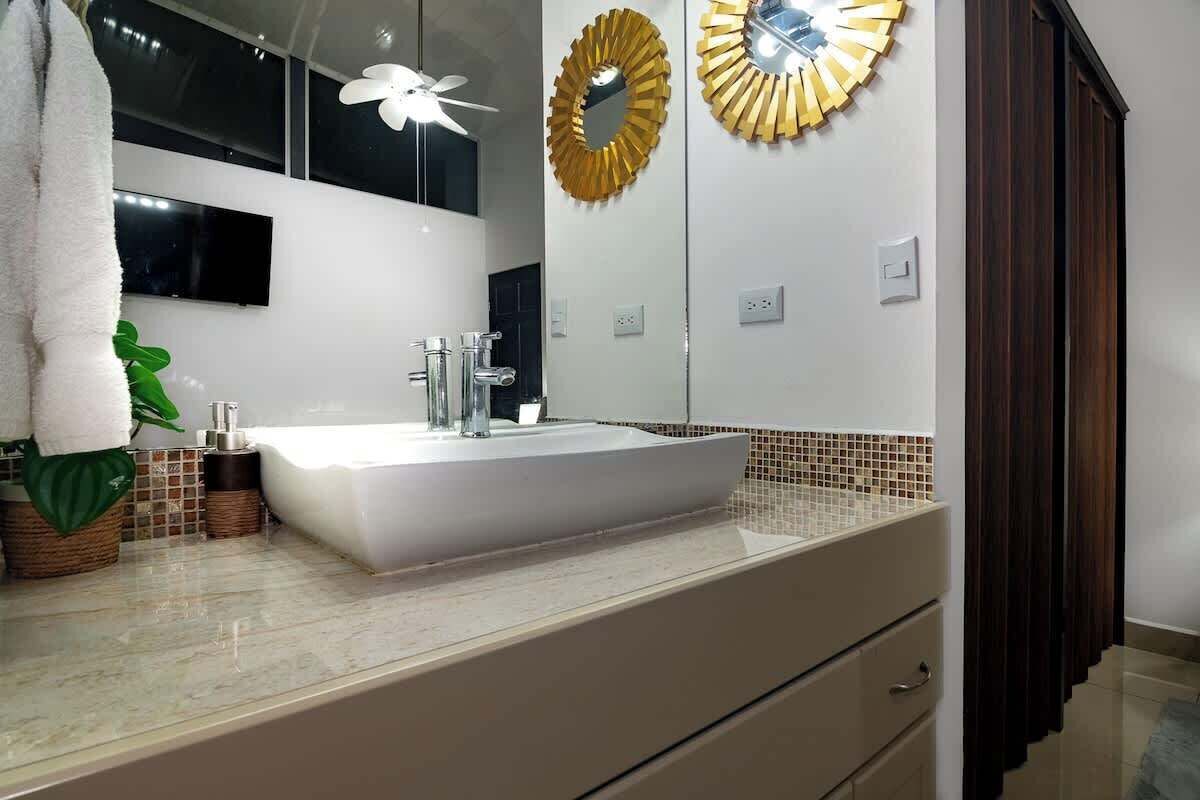 A bathroom with a white sink, a mirror, a ceiling fan, and a decorative gold mirror on the wall.