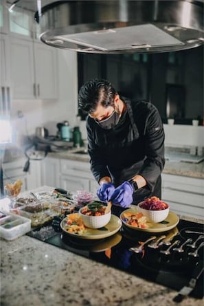 Eine Person bereitet Essen in einer modernen Küche mit Edelstahlgeräten und weißen Schränken zu.