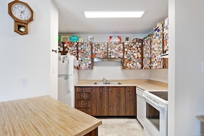 A compact kitchen with wooden cabinets, a built-in oven, and a refrigerator covered in stickers. - Cona Haven at Mount Washington (Mount Washington)