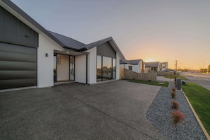 A modern building with large windows, a covered driveway, and a well-maintained lawn. - Modern 4BR with Billiards & Bright Living (Christchurch)
