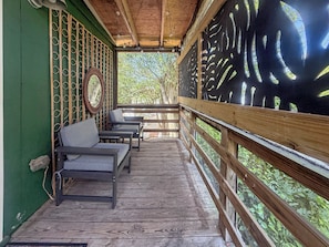 A wooden deck with a railing, a bench, and a wall with a circular mirror. - The Carriage House at Princess Place (Wilmington)