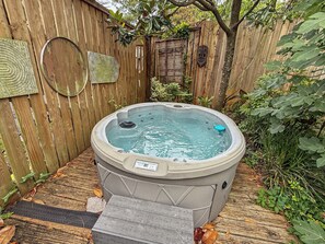 A hot tub in a backyard with a wooden fence, a wooden deck, and a small step leading up to it. - The Carriage House at Princess Place (Wilmington)