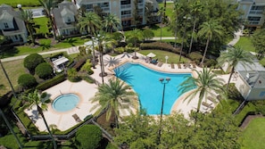 A large swimming pool surrounded by palm trees and lounge chairs, with a small circular pool nearby. - Brand New | 5Bd Villa w Pool, Spa & GameRoom 7832 (Kissimmee)