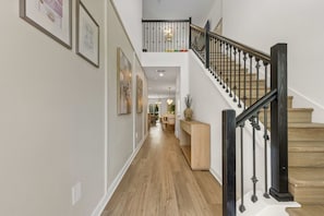 A hallway with a staircase, wooden flooring, and framed pictures on the walls. - Brand New | 5Bd Villa w Pool, Spa & GameRoom 7832 (Kissimmee)