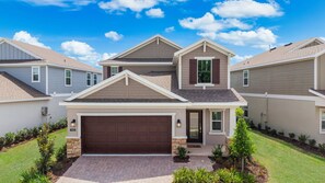 A modern residential building with a central garage, a small porch, and a well-maintained lawn. - Brand New | 5Bd Villa w Pool, Spa & GameRoom 7832 (Kissimmee)
