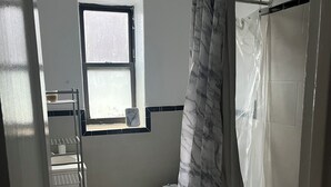 Ein Badezimmer mit Toilette, einem Fenster, einer Duschvorhang und einem Ablagebrett mit Pflegeprodukten.