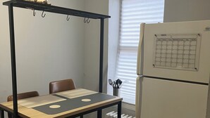 Eine Küche mit Tisch, Stühlen, einer Kleiderstange, einem Kühlschrank und einem Fenster mit Jalousien.