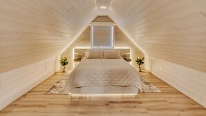Ein Schlafzimmer mit schrägverdeckter Decke, einem Bett, Nachttischen und einem Fenster.
