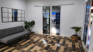 Une pièce avec un canapé gris, un parquet en bois, un grand miroir et deux plantes en pot.