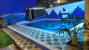 En swimmingpool med blå fliser og et geometrisk mønster, omgivet af en blå væg og et hegn.