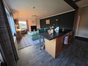 A modern kitchen with a central island, a dining area with a sofa, and a view of the outdoors. - Highlands - River View - Apt - Sleeps 4 - Garden (Garve)